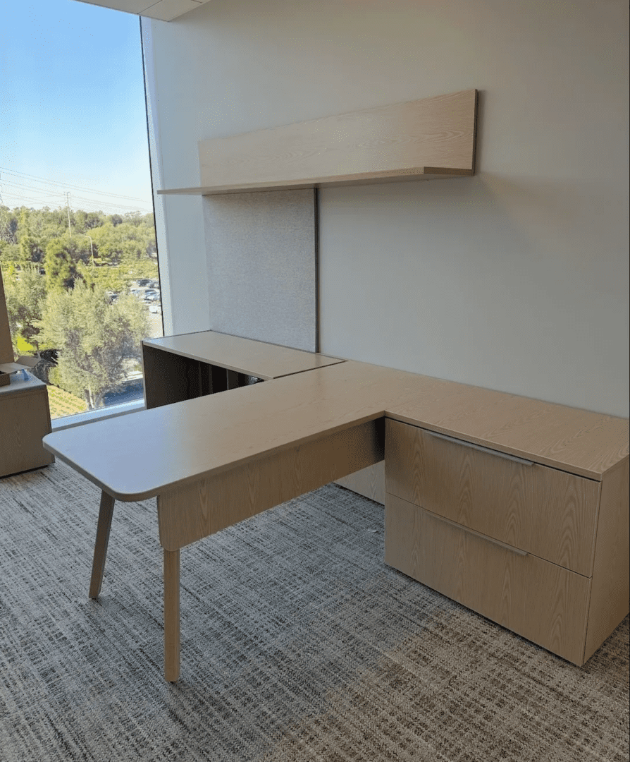Modern L-shaped office desk with drawers and a window view.